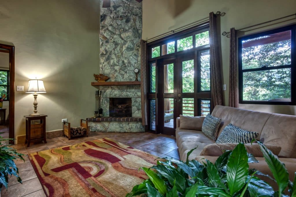 Cozy living room featuring a natural stone fireplace, a light sofa, and large windows with outdoor views.