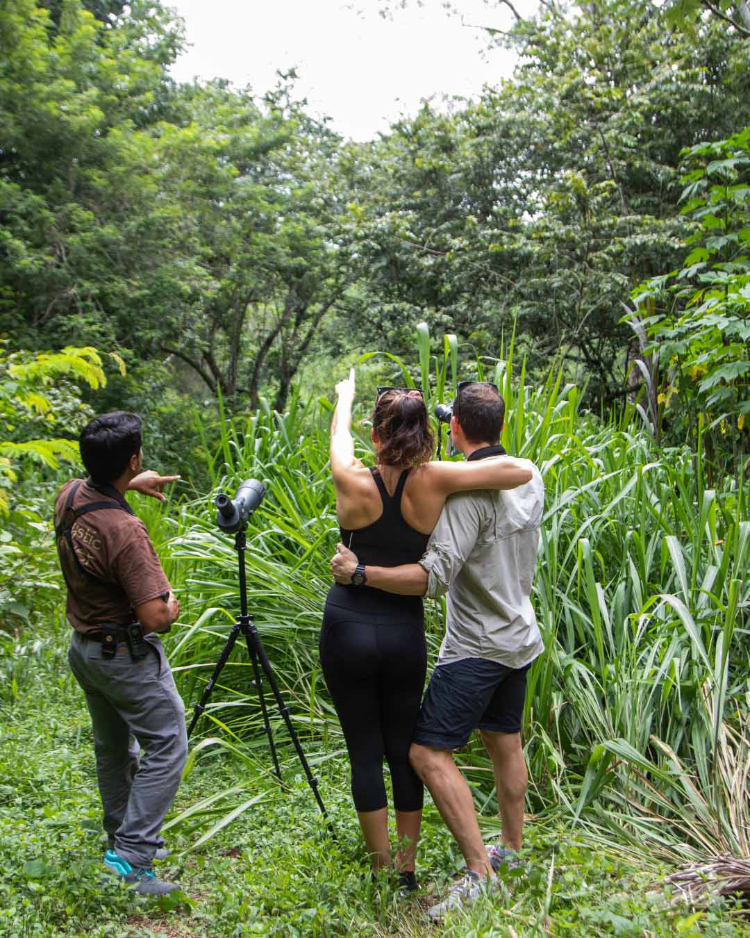 Three people in a lush green setting, observing nature with binoculars and a spotting scope.