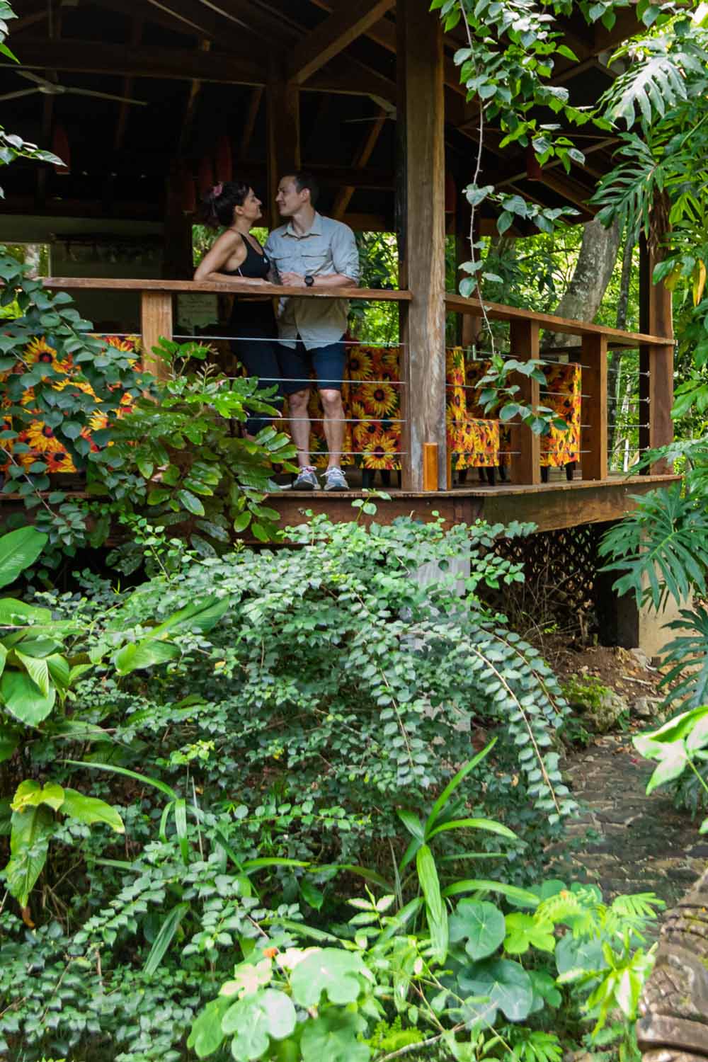 A couple embraces on a balcony surrounded by lush greenery.