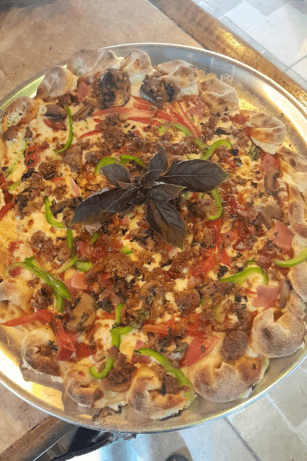 A savory pizza topped with vegetables, meats, and herbs, garnished with a sprig of basil.