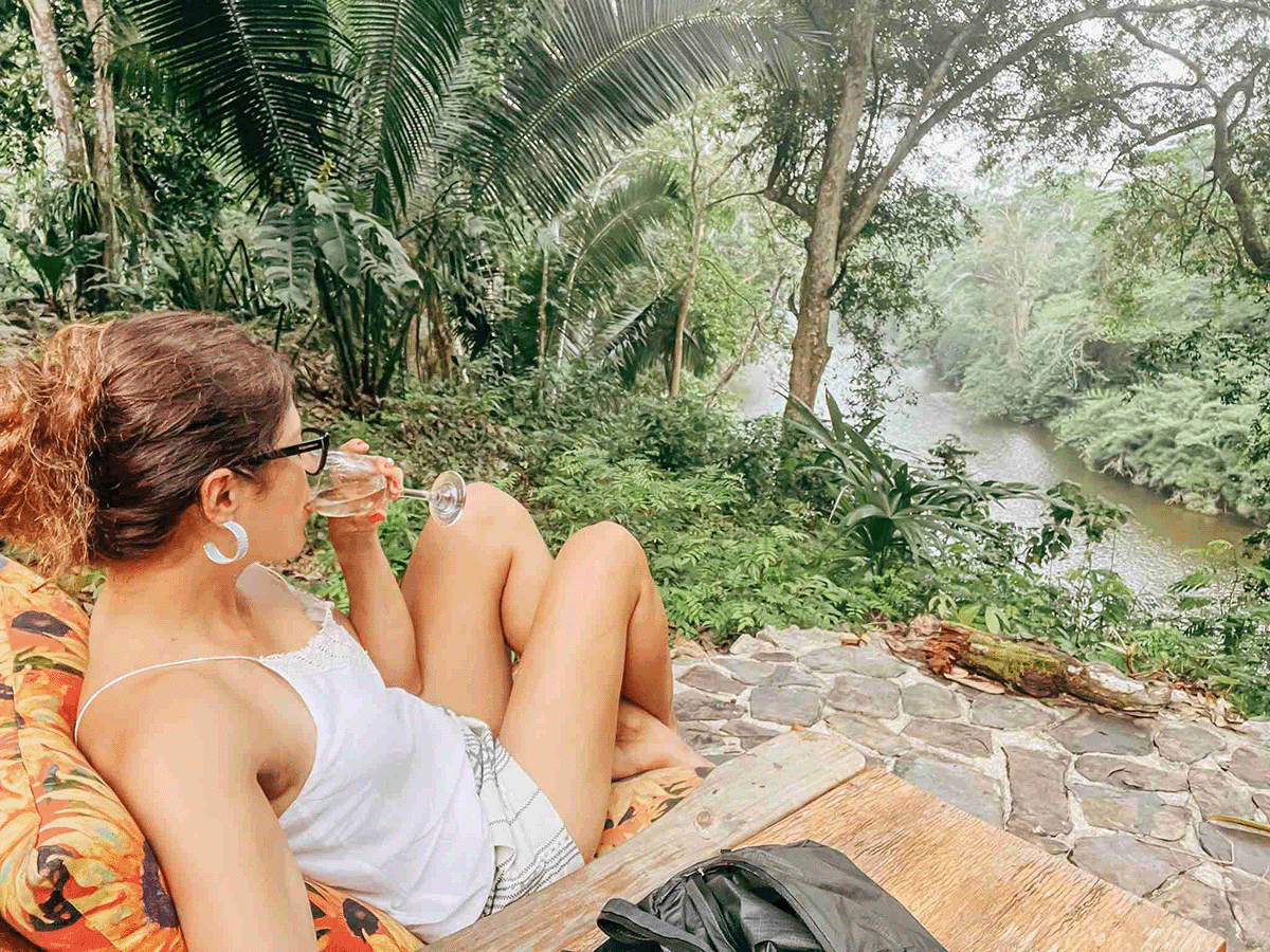 A person relaxes with a drink while enjoying a lush river view.