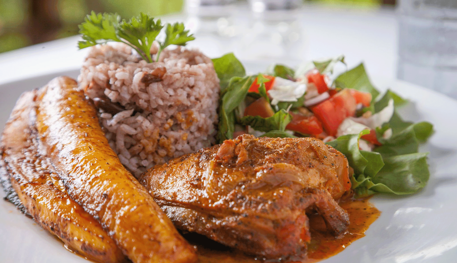 A plate of seasoned chicken, rice and beans, fried plantains, and a fresh salad.