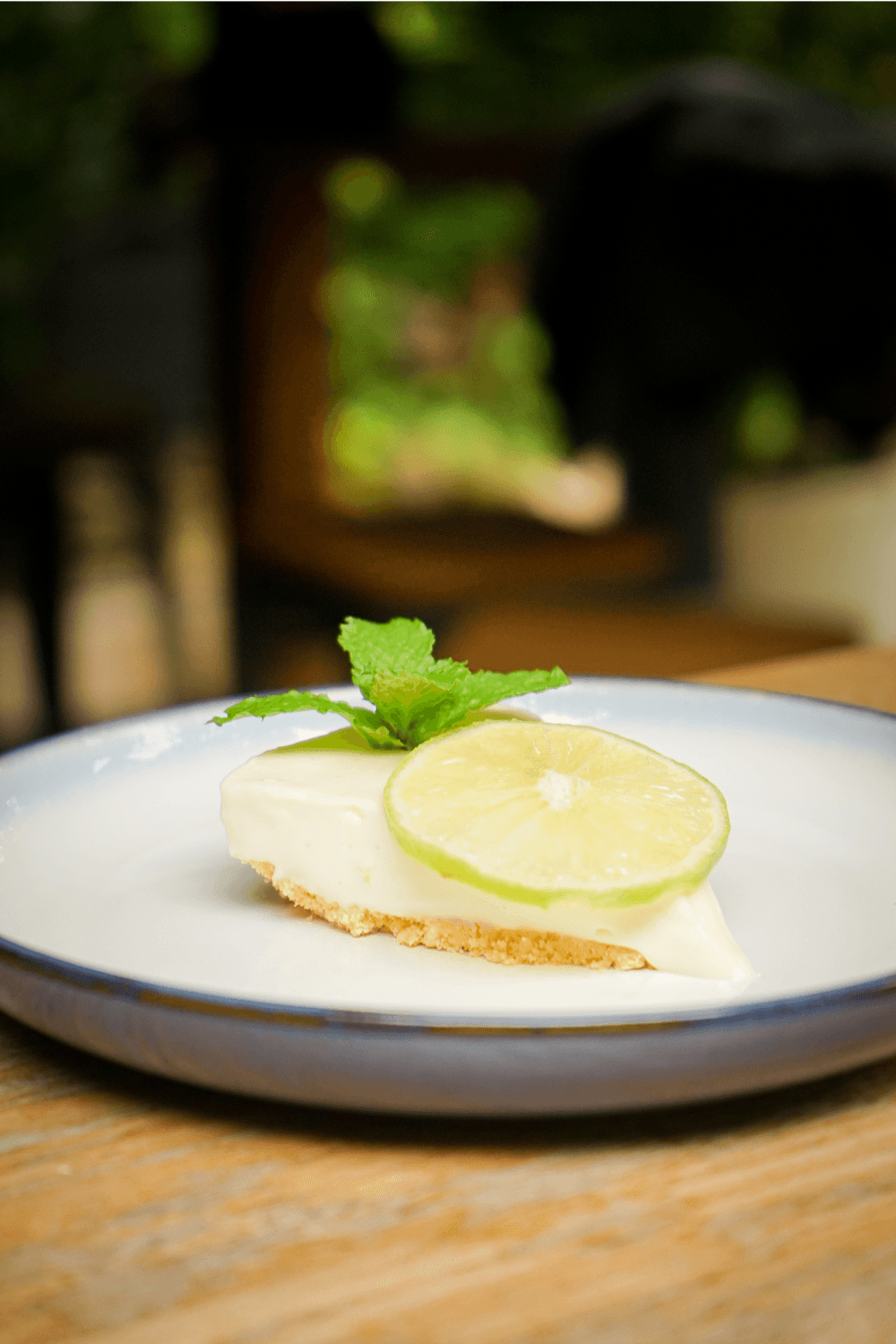 A slice of lime cheesecake garnished with a lime wheel and mint, served on a blue-rimmed plate.