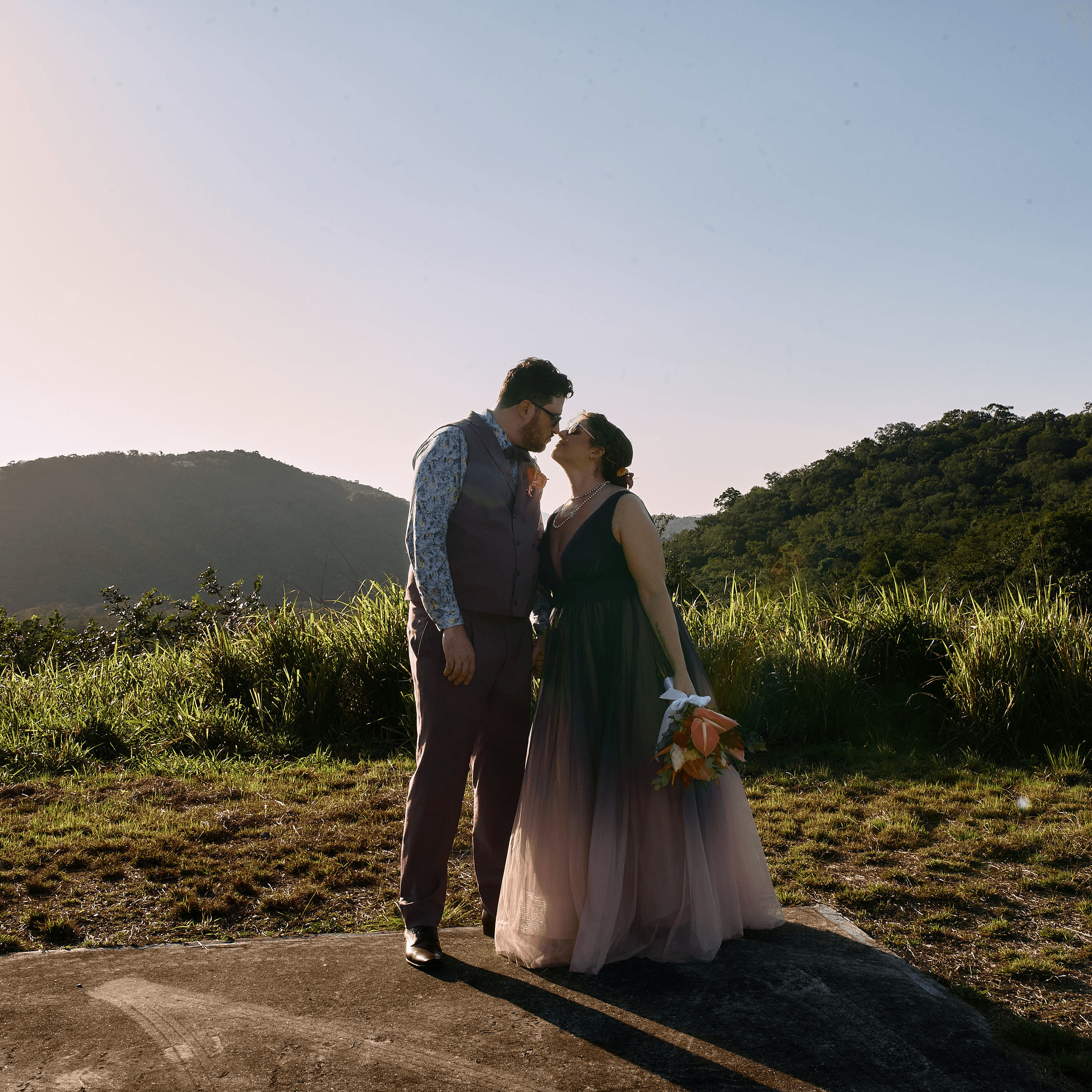 A couple shares a kiss against a scenic mountain backdrop during golden hour.