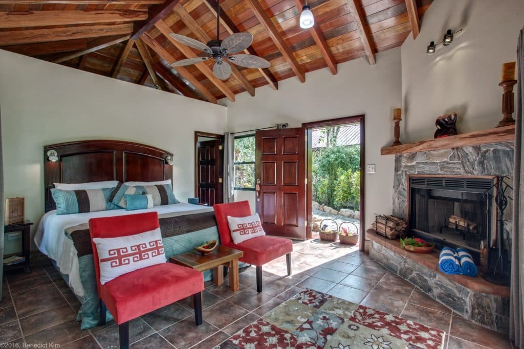 Cozy bedroom with a wooden ceiling, a fireplace, and red accent chairs.