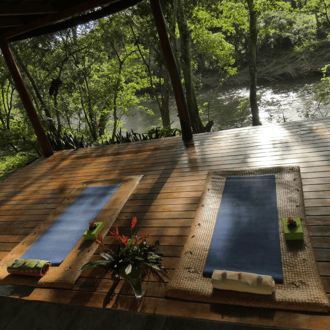 A peaceful outdoor spa area with two yoga mats overlooking a river, surrounded by greenery.