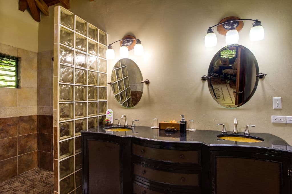A modern bathroom featuring a glass block shower, dual sinks, and decorative lighting.