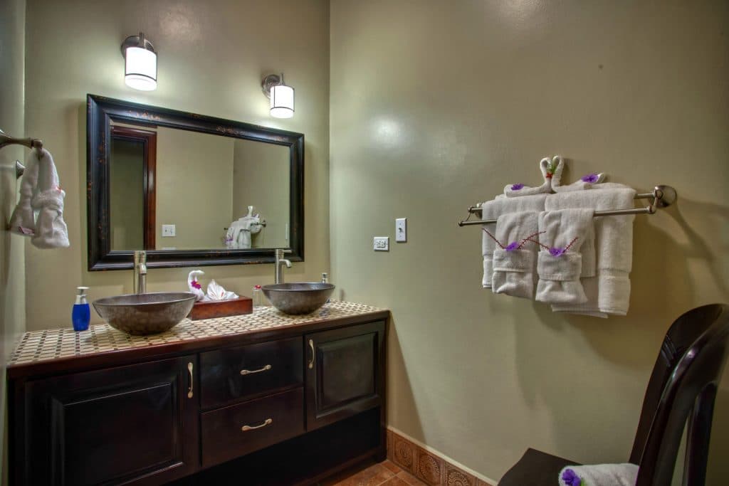 A modern bathroom featuring a dark vanity, two round sinks, decorative towels, and a large mirror.