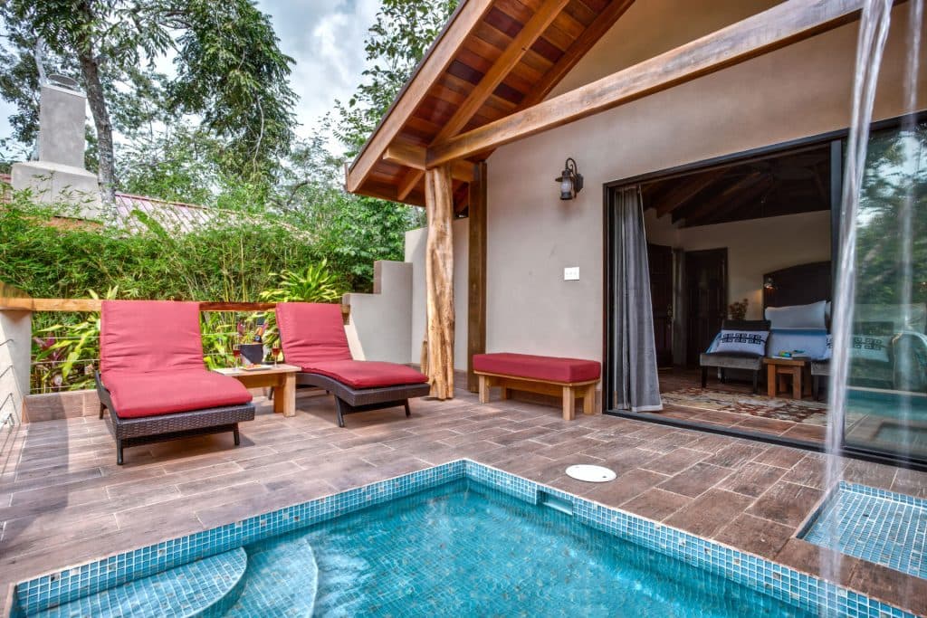 A cozy outdoor area with two red lounge chairs beside a small pool and a wooden cabin.