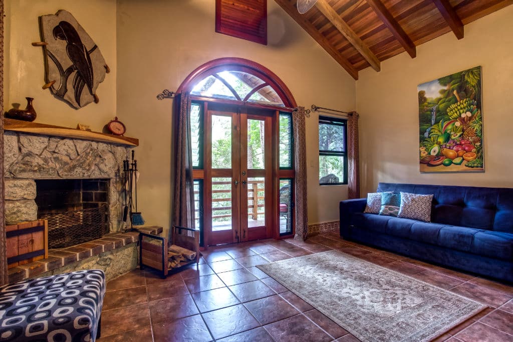 A cozy living room featuring a stone fireplace, large windows, and a blue sofa with decorative cushions.