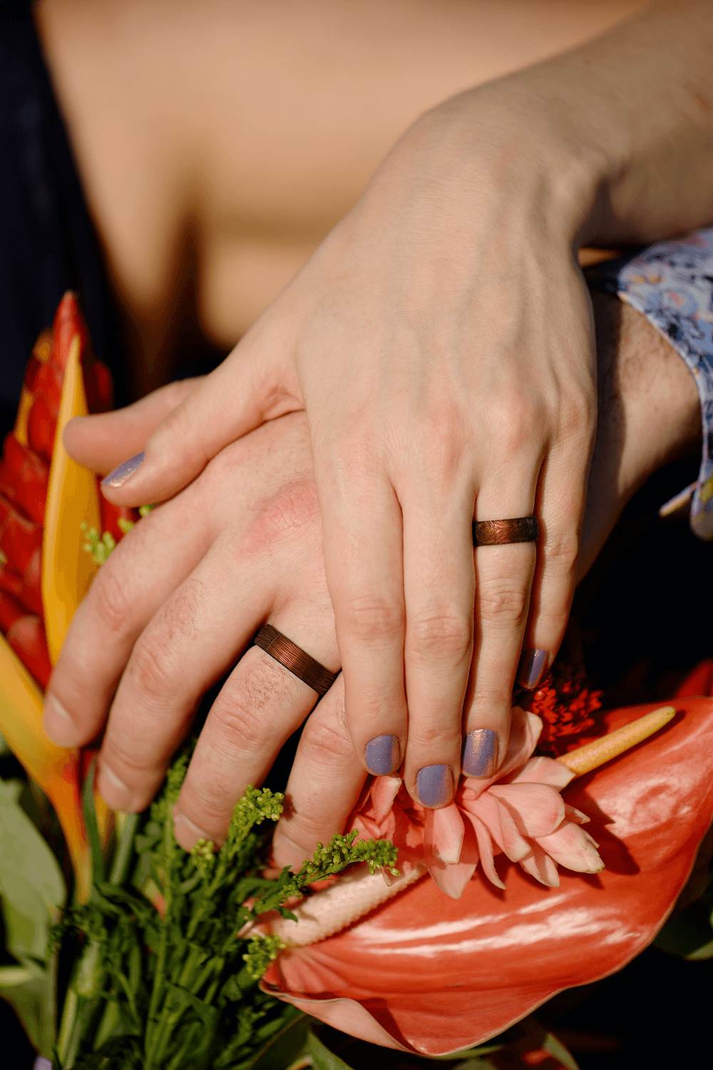 Two hands with matching rings are gently resting on vibrant flowers.