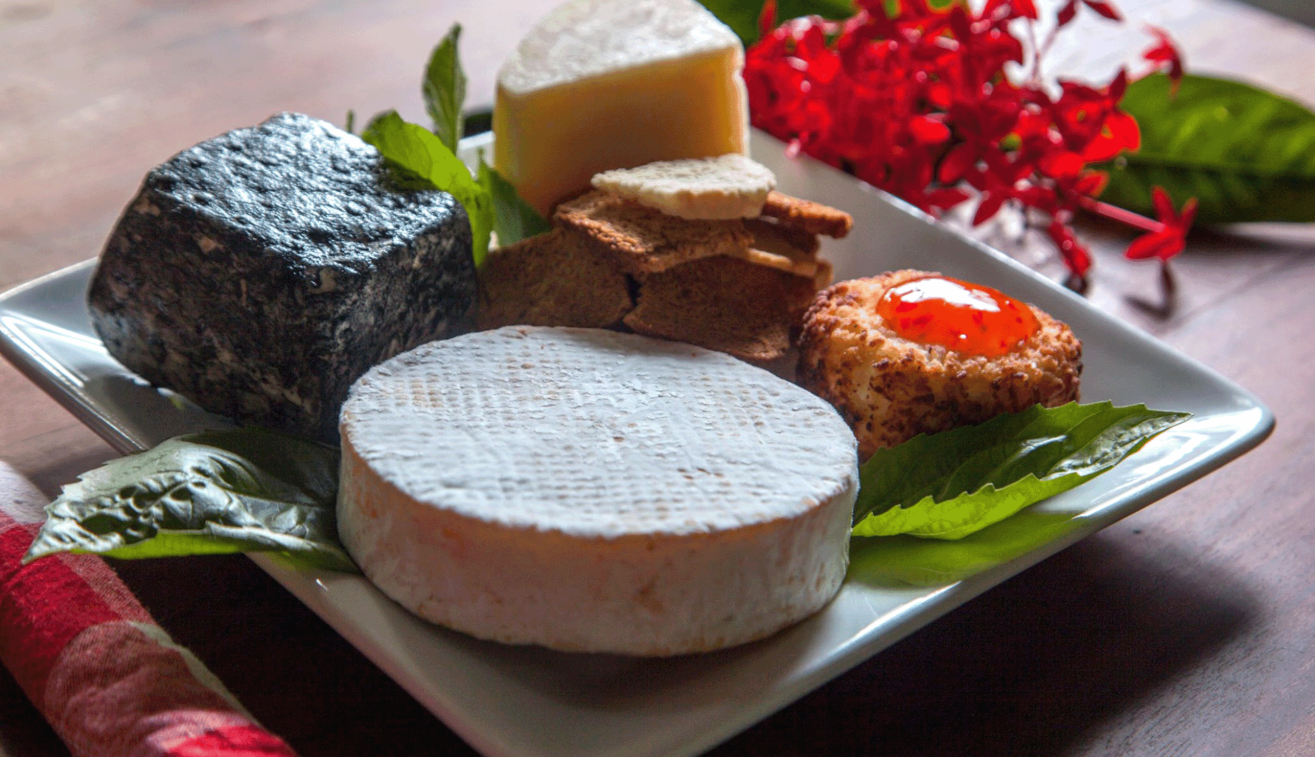 A selection of cheeses arranged on a plate with crackers and decorative leaves.