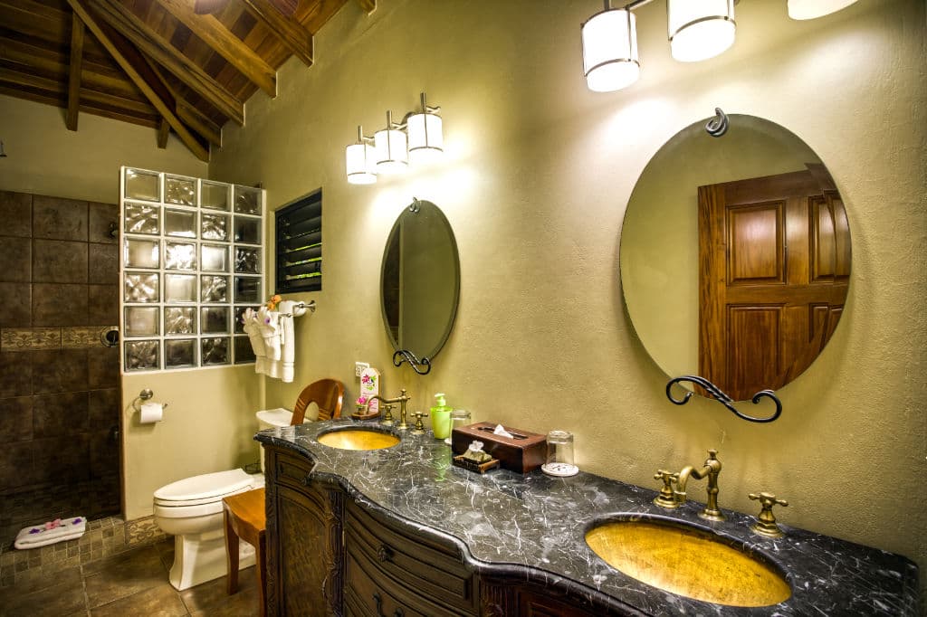 A stylish bathroom featuring a double sink vanity, mirrors, and a glass-block shower.
