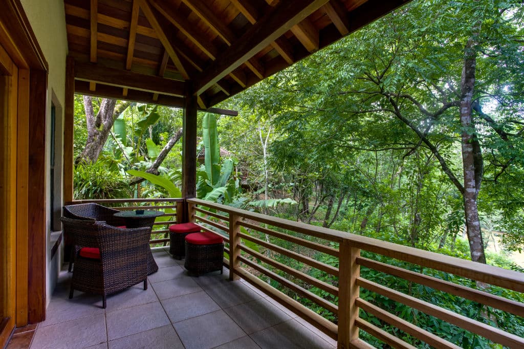 A cozy balcony with wicker furniture overlooks a lush green forest.