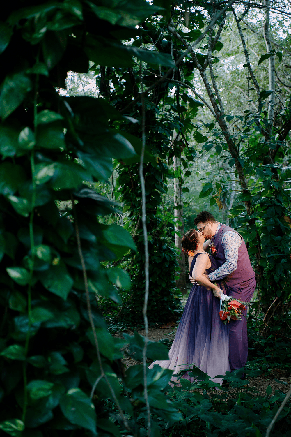A couple shares a kiss in a lush, green forest setting.